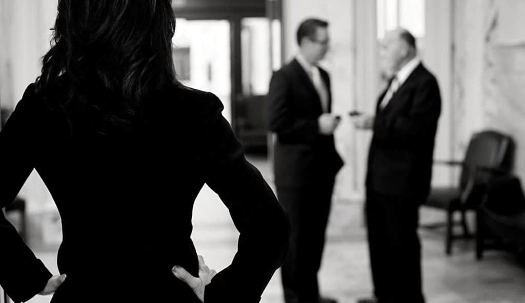 Woman in suit from behind looking at men talking 1680x969